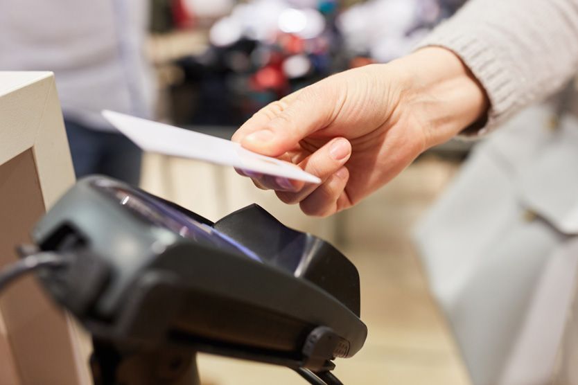 Es ist die Ansicht einer kontaktlosen Zahlung abgebildet. Eine Hand hält eine Bankkarte über ein NFC-Lesegerät.