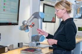 BMWK/ Mittelstand-Digital Zu sehen ist eine Frau, die einem Roboterarm einen Stift übergibt.