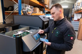 BMWK/ Mittelstand-Digital Zu sehen ist ein Mensch, der an einer Maschine ein Touchpad bedient und ein Smartphone in der Hand hält.