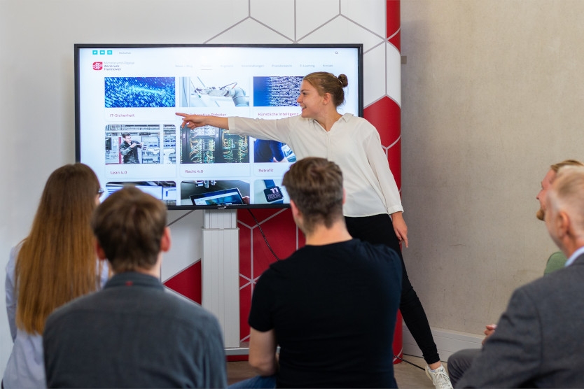 Junge Frau präsentiert vor Publikum an einem Monitor.