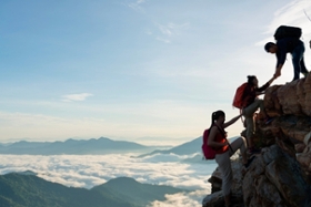 Drei Personen erklimmen einen Berg und helfen sich dabei gegenseitig