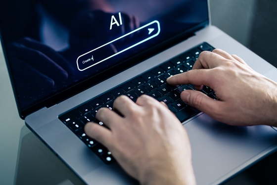 Hände tippen auf Laptop; auf dem Display ist Schriftzug "AI" zu sehen